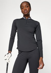 Melna garajām piedurknēm veiktspējas krekls ar ceturtdaļas rāvējslēdzēju, ar kontrastējošām svītrām ap apkakli, gludu tekstūru un pieguļošu dizainu.