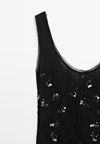 Robe noire sans manches avec un décolleté en U, ornée de dentelle florale et de paillettes argentées dispersées sur un tissu transparent.