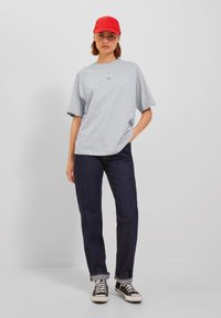Grå oversized t-skjorte med korte ermer og en liten logo, mørkeblå straight-leg jeans, og svarte høye sneakers med hvite snørebånd. Rød caps på toppen.