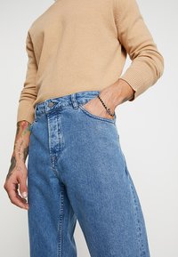 Jeans de mezclilla azul claro con cintura alta, que cuentan con cinco bolsillos, un cierre de botón metálico y un sutil efecto desgastado.