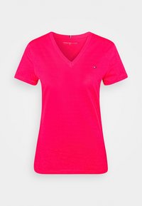Camiseta de algodón de color rosa con escote en V, que presenta mangas cortas y un pequeño emblema en el pecho. Textura suave con un diseño ajustado.