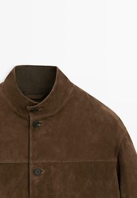 Braune Wildlederjacke mit hohem Kragen und drei sichtbaren schwarzen Knöpfen auf der Vorderseite, dargestellt vom oberen Torso-Bereich.