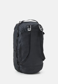 Svart tygryggsäck med cylindrisk form, med vit sömnad, topphandtag och justerbara remmar. Hållbart material med dragkedjor.