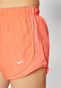 Nike šorti spilgti korālā krāsā, izgatavoti no viegla auduma ar sietveida sānu paneli. Iezīme elastīga josta un balta emblēma.