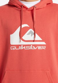 Korálová mikina z bavlneného zmesi s prednou kapsou, s bielym logom Quiksilver a vzorom hory. Kapucňa so sťahovacími šnúrkami a kovovými koncami.