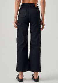 Črne široke hlače iz trdnega materiala, z visokim pasom, zadnjimi žepi in usnjeno etiketo na pasu.