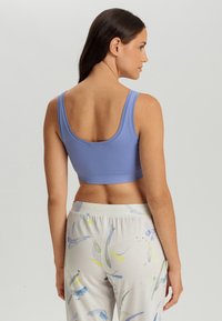Hellblauer Sport-BH mit rundem Ausschnitt, breiten Trägern und figurbetontem Design. Kombiniert mit lässigen, gemusterten Hosen in Pastellfarben.