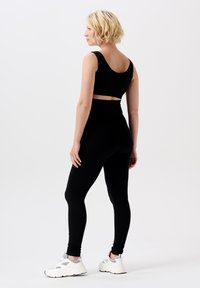 Ensemble de fitness noir à côtes comprenant un haut court avec de larges bretelles et un legging taille haute. Accompagné de baskets blanches avec des accents gris.