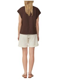 Brown short-sleeve top paired with white, rolled-up shorts. Sandals with a brown strap. Straight cut shape, minimal detailing.