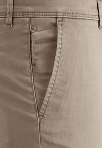 Pantalon en mélange de coton beige avec un front plat, poches latérales diagonales, coutures visibles et texture lisse. Design ajusté pour une silhouette cintrée.