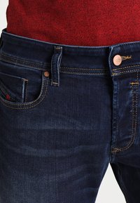 Mörkblå jeans i denim med femficksdesign, kopparfärgad hårdvara och kontrasterande gul sömnad.