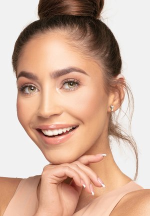 Giovane donna con lunghi capelli castani raccolti in un bun, che indossa orecchini d'argento e un top nude, sorridente, con pelle chiara e trucco leggero.