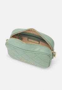 Quilted green faux leather bag with gold zipper and logo, featuring a spacious interior and smooth texture. Opens at the top.