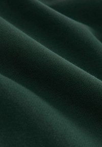 Tissu vert foncé avec une texture tricotée serrée, présenté en plis doux sous un éclairage diffus.