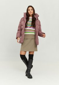 Puffy mauve outer jacket, white and multi-striped sweater, beige skirt, black knee-high boots with chunky soles, standing on a light background.