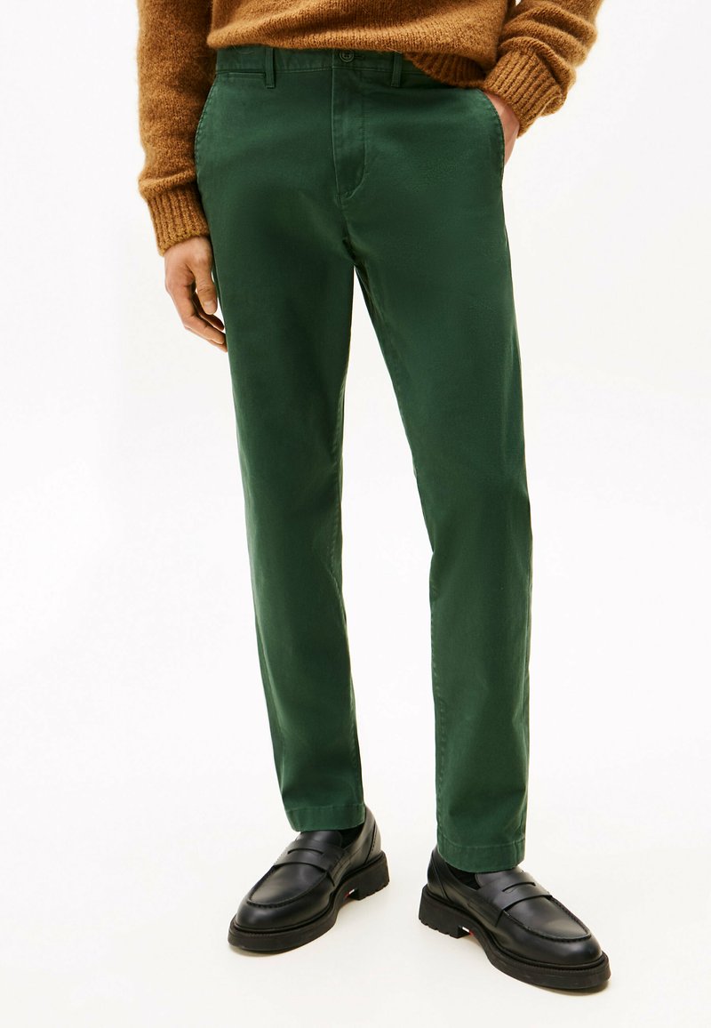 Zielone, dopasowane spodnie wykonane z gładkiego materiału, z zapięciem na guziki i bocznymi kieszeniami, w połączeniu z czarnymi mokasynami.