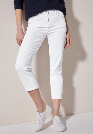 Jeans blancos recortados de mezclilla, con un ajuste slim, bolsillos frontales y cierre de botón. Combinados con zapatillas blancas con cordones.