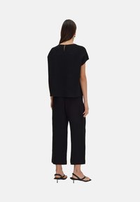 Zwart cropped top met korte mouwen en een keyhole rug, gecombineerd met zwarte brede broek. Beide hebben een gemêleerde stof. Zwarte enkelbandhakken.