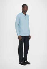 Lys blå langermet skjorte med rund nakke og glidelås delvis. Sammen med mørkeblå denimbukser og svarte sko.