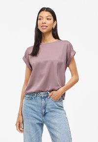 Lavender short-sleeve top with a round neckline, made of smooth fabric, paired with light blue high-waisted jeans. Features rolled cuffs.