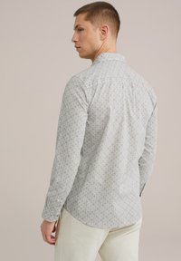 Camisa de color claro con un patrón geométrico repetido, cuello abotonado y mangas largas. El material parece tejido, con una textura suave.