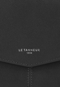Cartera de cuero negro con una textura suave, costuras sutiles y un logotipo plateado que dice "LE TANNEUR 1898" en la parte inferior.
