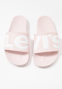 Paire de sandales roses clair à enfiler avec de larges brides comportant de grandes lettres blanches du logo Levi's.