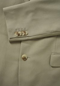 Tissu de blazer beige clair avec une texture lisse. Comprend une manchette à quatre boutons avec des boutons de couleur claire et un seul bouton à l'avant.