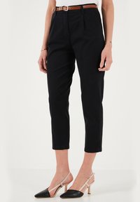 Pantaloni a cropped neri con vita alta, realizzati in tessuto liscio. Presentano una cintura marrone abbinata e sono abbinati a tacchi a punta neri e beige.