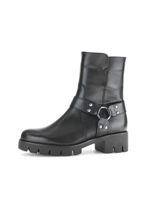 Stivale alla caviglia in pelle nera con suola spessa, caratterizzato da una cinturino laterale con fibbia e dettagli borchiati. Texture liscia e design elegante.