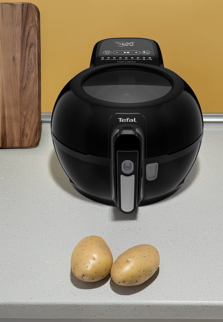 Schwarze Tefal Heißluftfritteuse mit transparentem Deckel und digitalem Display, auf einer hellen Arbeitsplatte neben zwei ungeschälten Kartoffeln platziert.
