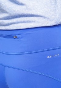 Leggings Dri-Fit blu con texture liscia, tessuto elasticizzato, dettagli di cucitura visibili e una piccola tasca con zip sulla cintura.