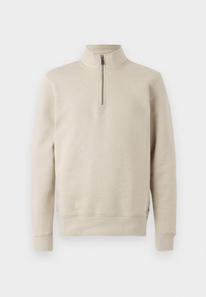 Sweatshirt beige à col montant et fermeture à demi-zip. Fabriqué en tissu doux avec des poignets et une taille côtelés, présentant une texture lisse.