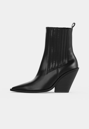 Bottine noire en cuir à bout pointu, avec un empiècement latéral côtelé, une boucle d’enfilage et un talon épais incliné.