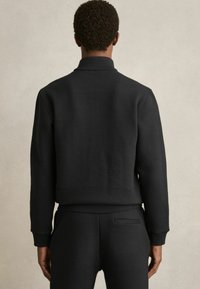 Pulover negru cu cusături ribbate, guler înalt și mâneci lungi, având o talie ajustată și un material neted, texturat. Design simplu.