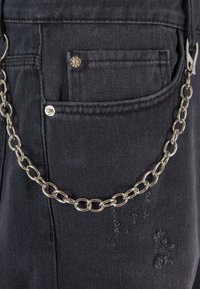 Čierne džínsy z denimu so strieborným reťazcom pripevneným k pravej kapse. Významné detaily zahŕňajú malú prednú kapsu a jemné známky opotrebenia.