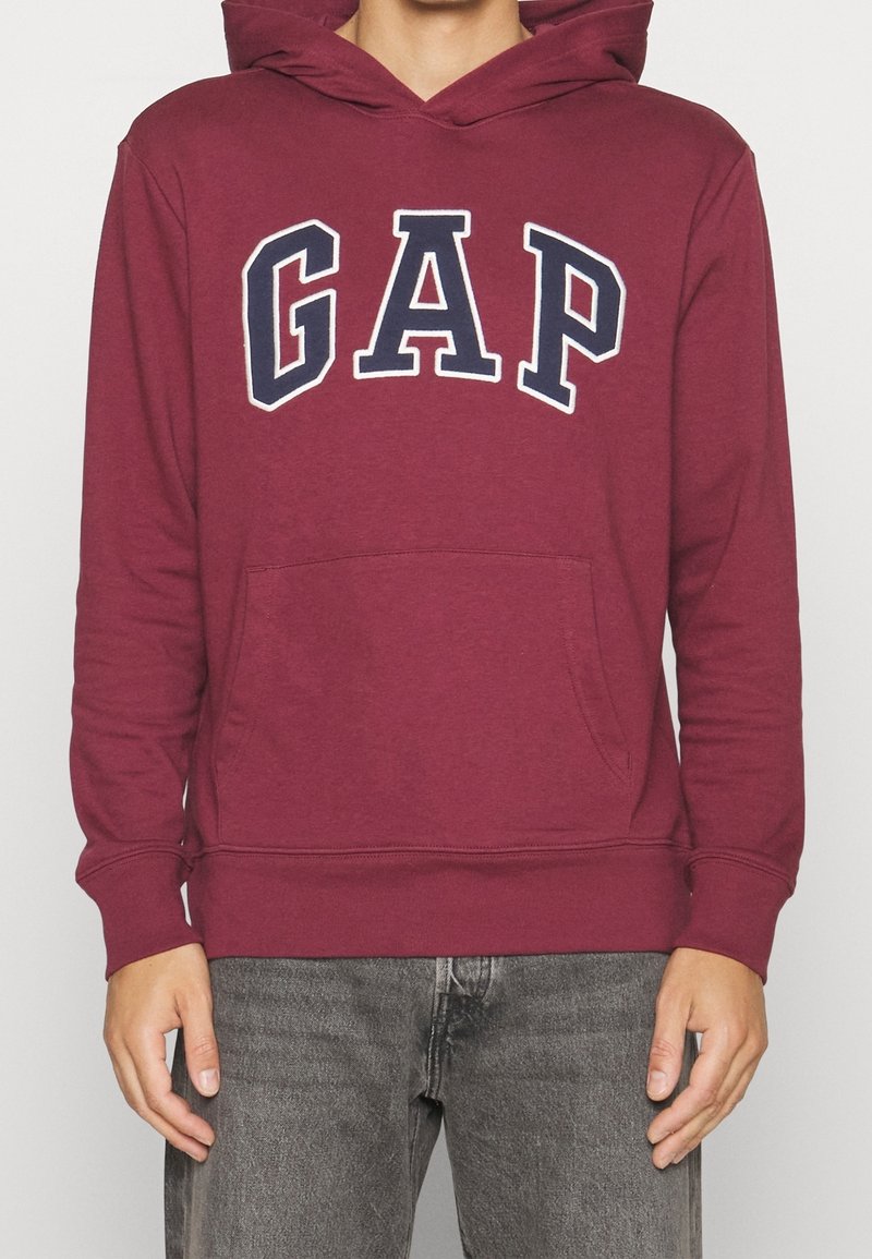 Bordowa bluza z kapturem z dużym białym i granatowym logo „GAP”, kieszenią kangurką, kapturem na sznurki oraz ściągaczami na mankietach i na dole.