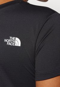 Musta lyhythihainen T-paita, jossa valkoinen "The North Face" -logo yläselässä, valmistettu sileästä ja kevyestä kankaasta.