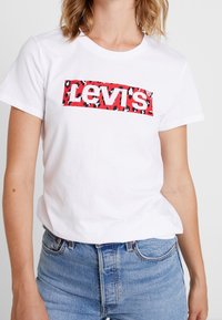 T-shirt bianca in cotone con un rettangolo a stampa leopardata rossa e nera e la scritta "Levi's" in bold bianco sul petto. Maniche corte.