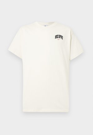 Camiseta de algodón color crema con mangas cortas, que presenta "NIKE SB" en texto negro y rojo en el pecho. Cuello redondo estándar.