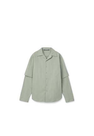 Camicia verde chiaro a maniche lunghe con bottoni, tasca frontale e maniche a strati su sfondo bianco.