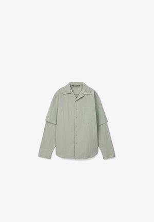 Chemise à manches longues vert clair avec boutons, une poche avant et des manches superposées sur fond blanc.