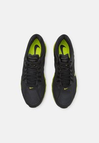 Sapatilhas desportivas pretas com parte superior em malha, detalhes amarelos e palmilha verde. Apresentam atacadores e um logótipo proeminente. Biqueira arredondada e sola almofadada.