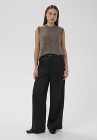 Svetlo rjava brezrokavnik iz pletenine, kombiniran z visokim pasom črne hlače širokih hlačnic. Hlače imajo pregibani dizajn in črni pas.