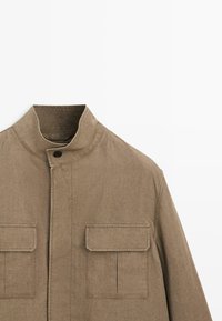 Braune Jacke mit hohem Kragen und Knopfverschluss sowie zwei großen aufgesetzten Fronttaschen aus strukturiertem Stoff.