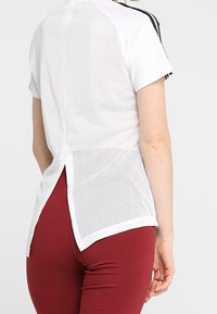 Vit sporttop med meshbak, korta ärmar och svarta ränder. Har en delad nederkant för ökad ventilation och rörelse.