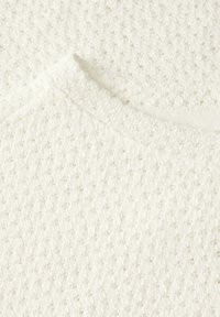 Vitt stickat tyg med ett texturerat mönster av små hål. Urringningen har en mjuk, slät finish som förbättrar den övergripande designen.