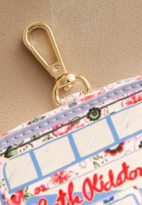 Õielise mustriga tõmblukuga kotike kuldse metallist klambriga. Omab helesiniseid ja roosasid aktsente, siledat tekstuuri ning õmmeldud servasid.