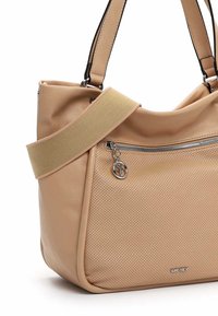 Sac à main en cuir beige avec poche avant perforée, fermeture éclair argentée et breloque, de marque "Suri Frey," et large bandoulière en tissu.