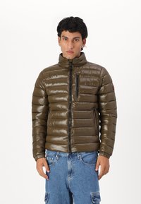 Veste puffy vert olive, matériau léger et brillant, col montant, poche poitrine zippée, poignets élastiques, ourlet côtelé, motif matelassé.